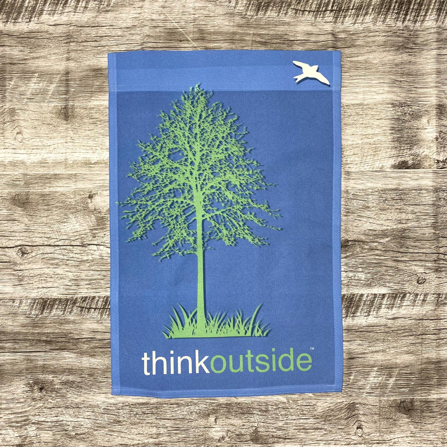 Periwinkle blue garden flag featuring a bright green silhouette of a tall tree and a bird with the phrase Think Outside.