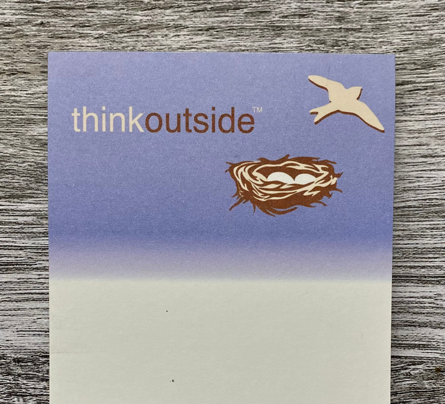 A notepad of 50 sheets of white paper featuring a violet blue sky with a bird flying out of a bird's nest with eggs.. The phrase Think Outside is printed beneath the image.