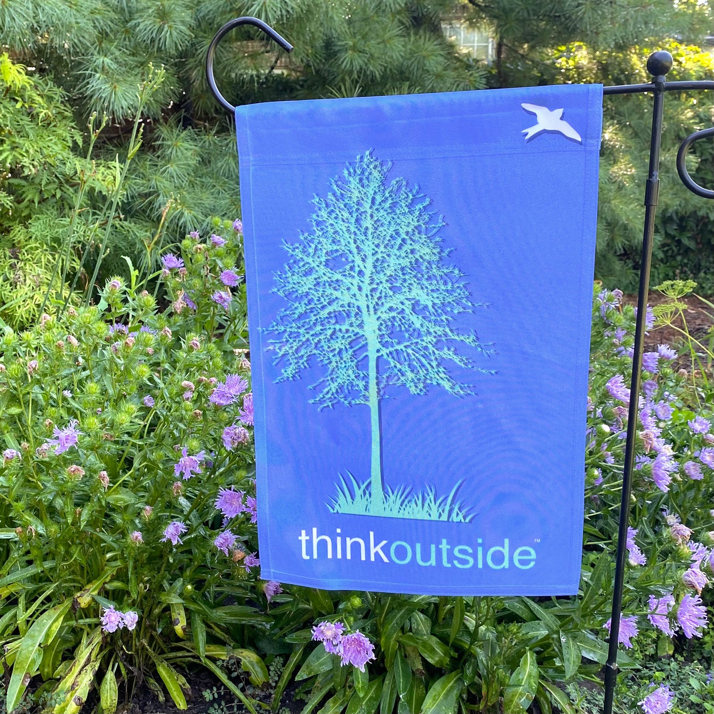 Periwinkle blue garden flag featuring a bright green silhouette of a tall tree and a bird with the phrase Think Outside.