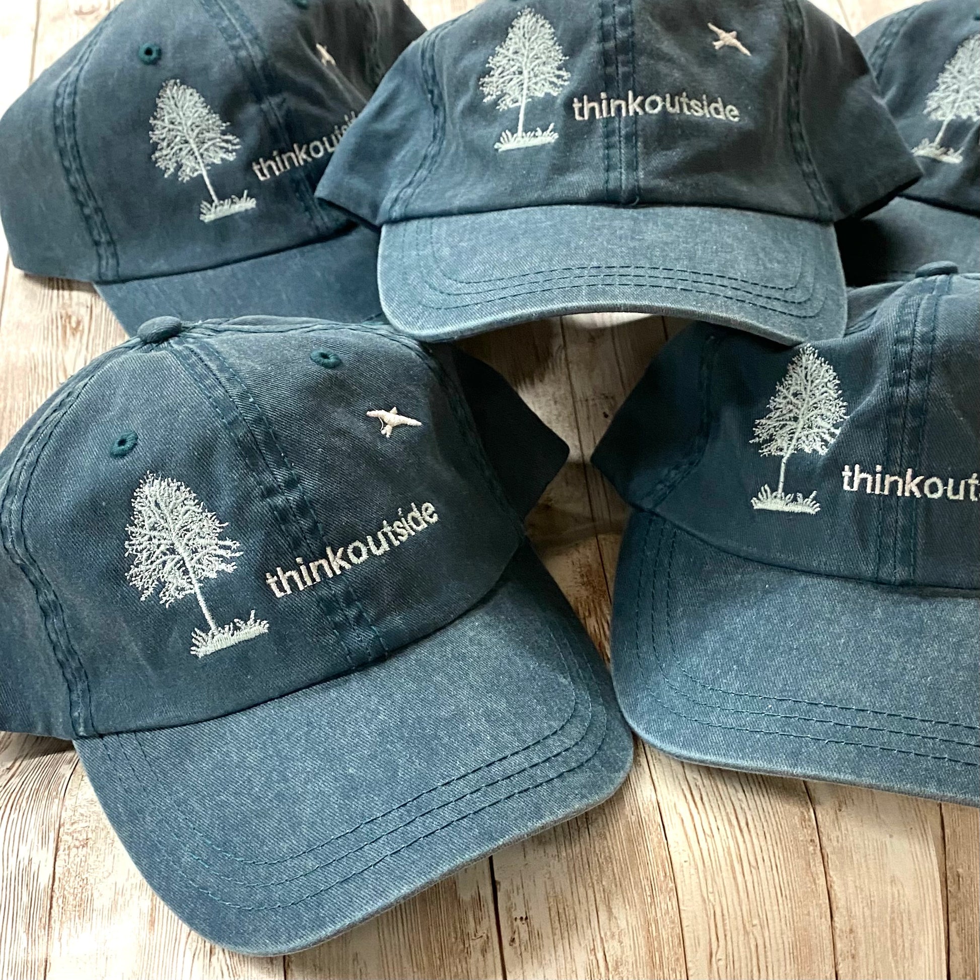 Heather deep green garment washed low profile baseball cap with a white embroidered silhouette of a tree and bird and the words Think Outside.