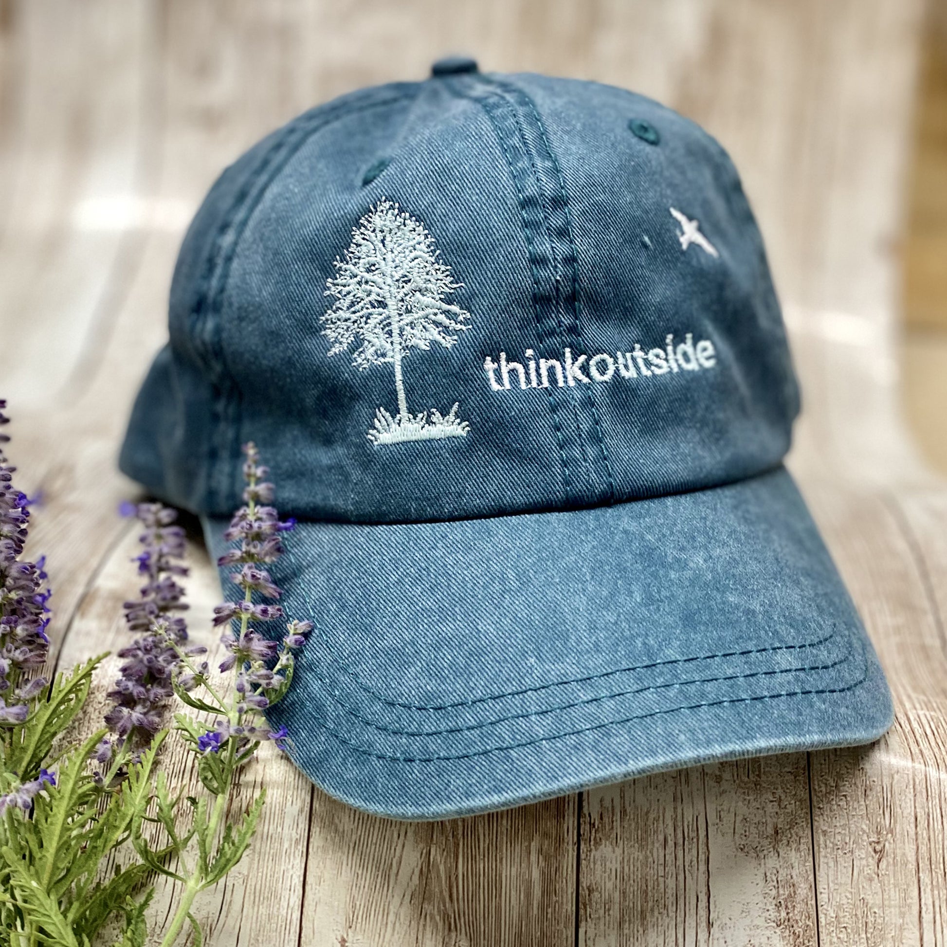 Heather deep green garment washed low profile baseball cap with a white embroidered silhouette of a tree and bird and the words Think Outside.