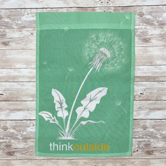 Dandelion seeds blowing in the wind on a colorful green garden flag for the backyard with the phrase Think Outside.