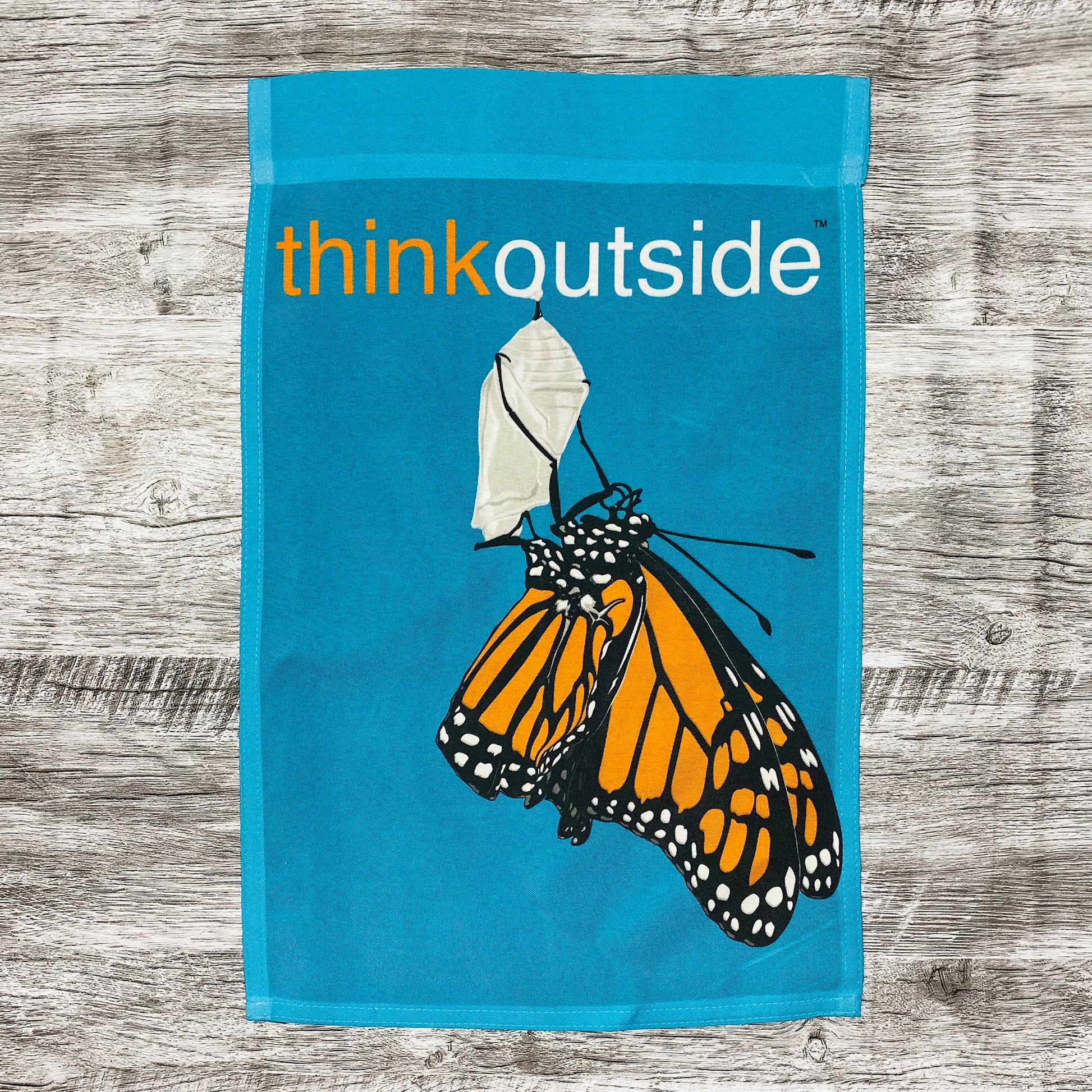 Bright teal garden flag with a large monarch butterfly clinging to its shell with the phrase Think Outside.