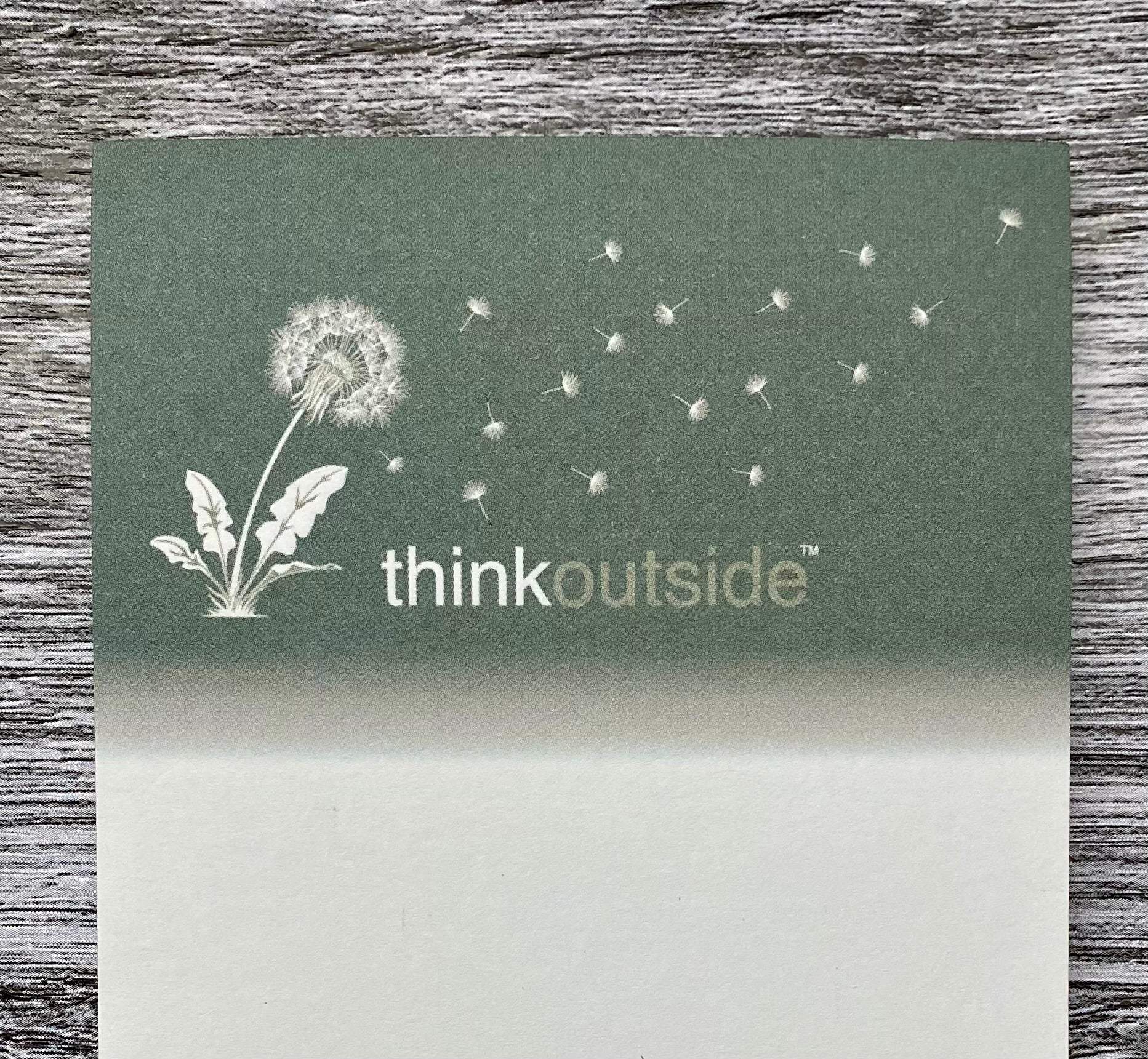 A notepad of 50 sheets of paper featuring a drawing of dandelion seeds blowing in the wind.  It also includes the phrase Think Outside