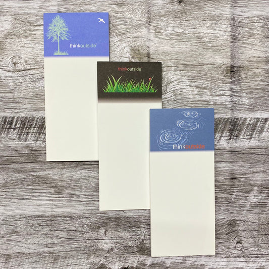 Three nature inspired notepads  each with 50 sheets of paper, one featuring the silhouette of a tree, one with blades of grass and a ladybug, one with rocks skipping on water.  All include the phrase Think Outside