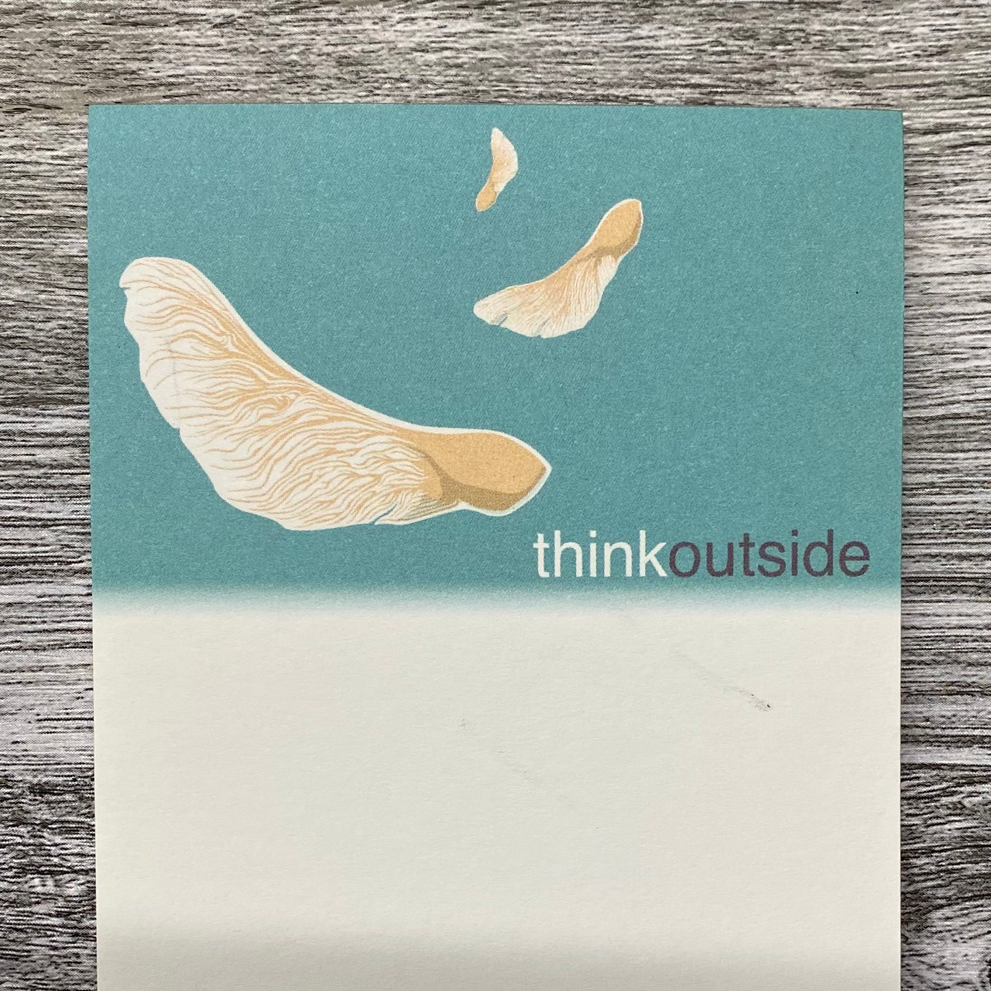A nature inspired notepad of 50 sheets featuring a drawing of maple seeds spinning in the air. It also includes the phrase Think Outside.