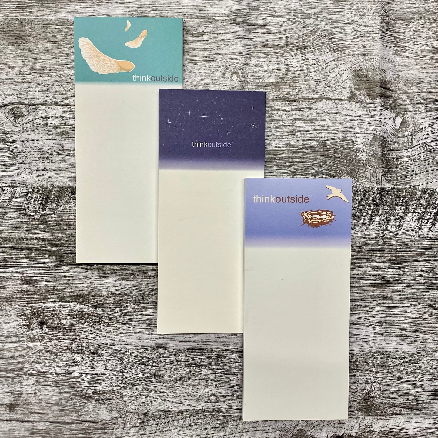 Three nature inspired notepads of 50  sheets each, one featuring maple seeds spinning in the air, one with the big dipper on a deep navy sky, and one with a bird's nest of eggs .  All include the phrase Think Outside.