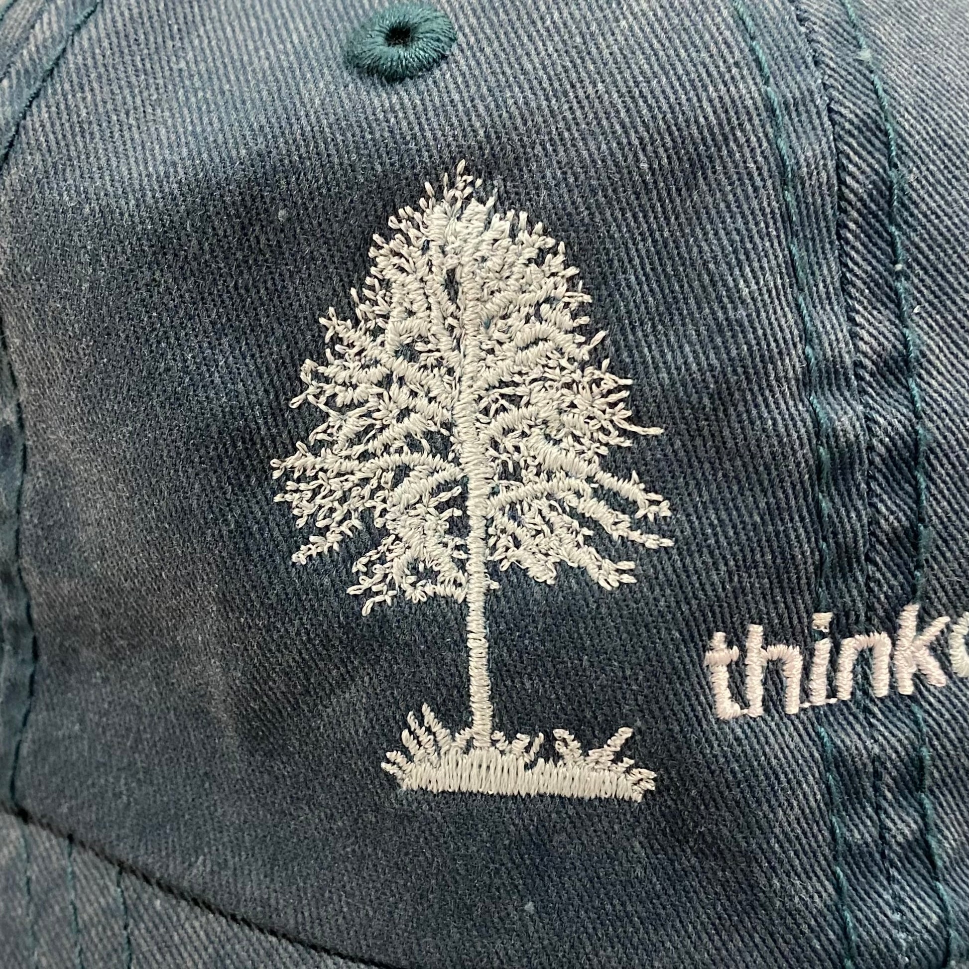 Heather deep green garment washed low profile baseball cap with a white embroidered silhouette of a tree and bird and the words Think Outside.